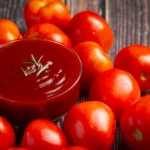 Koľko kečupu vznikne z 1 kg paradajok a koľko paradajok treba na pohár? Domáci kečup v miske obklopený zrelými červenými paradajkami