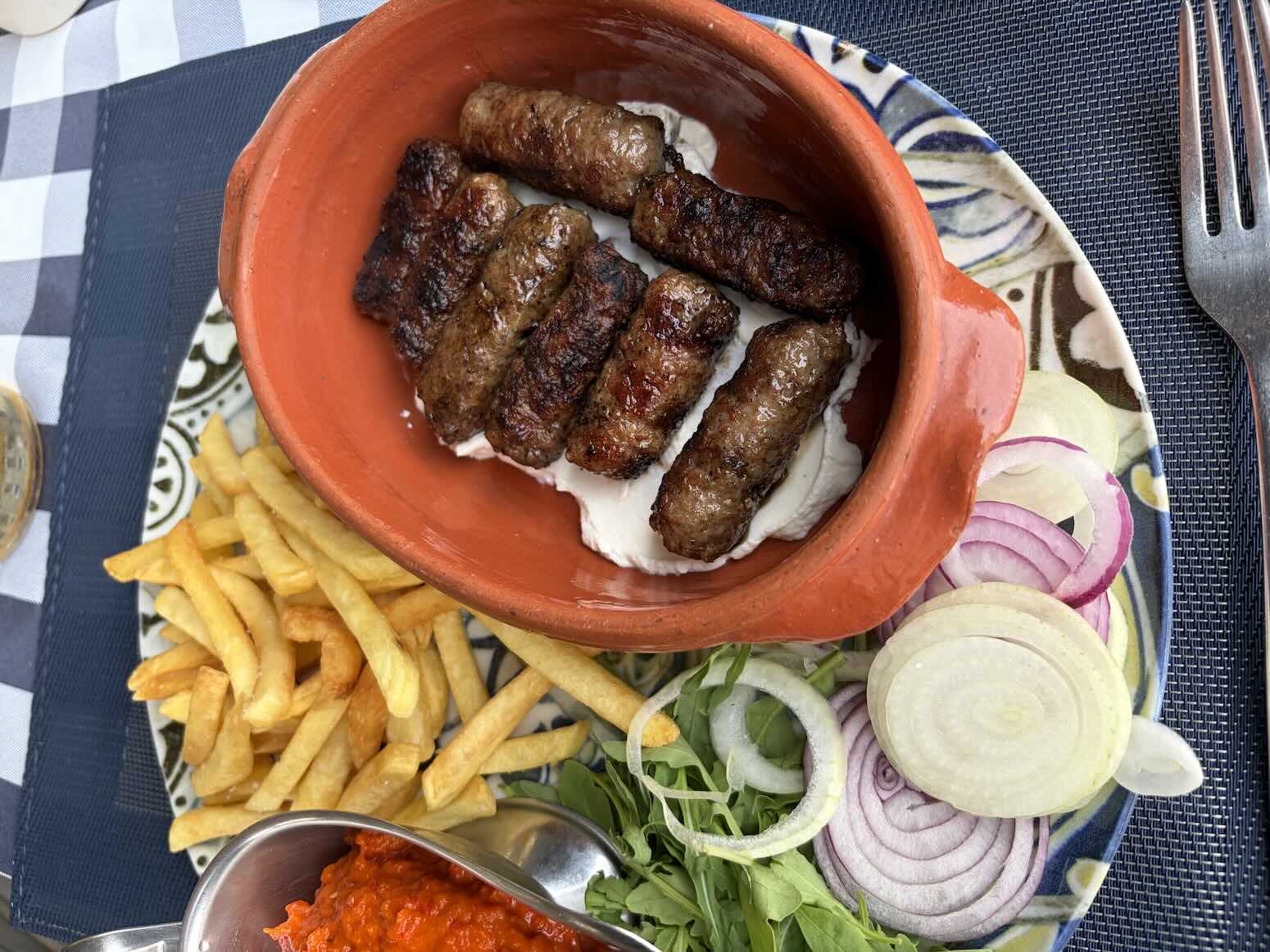 Čevabčiči s hranolkami, cibuľou a krémovou omáčkou na tanieri